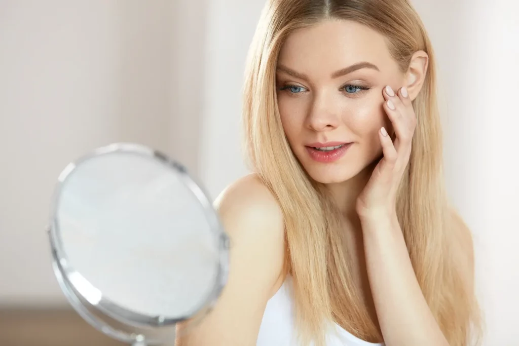 a portrait of a woman checking her face in front of the mirror after exosomes treatment